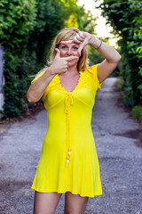 Portrait of Attractive Young Mother in Yellow Dress Standing in Public Park and Making a Finger Frame with her Fingers.