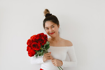 Asian Thai woman holding red roses, Happy smiling showing flowers and looking at camera, standing isolated over white background wall. 