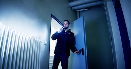 Mature Male Security Guard With Flashlight Standing In Corridor