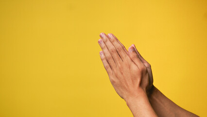 Men's hands praying and begging God for forgiveness on a yellow background
