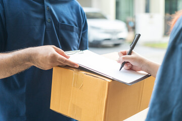 Delivery man holding a cardboard box while woman putting signature in clipboard. Hand female accepting a delivery boxes of paper containers from delivery man. Signing to get package. Delivery concept.