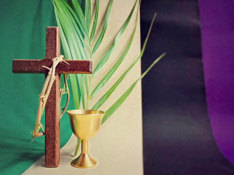 Holy Week, Lent Season, Palm Sunday, Maundy Thursday, Good Friday, Easter Sunday Concept - crown of thorns om wooden cross with chalice and palm leaf in multicolor background.