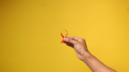 hand holding a red HIV ribbon on a yellow background