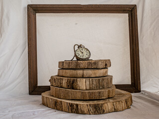 Antique decayed pocket watch on tree trunk rings with wooden frame on dirty white cloth background.