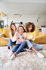 Vertical photo three young multi-ethnic women playing video games together at home. Group girls enjoying free time with popcorn in community in living room. Generation z and positive friendships.