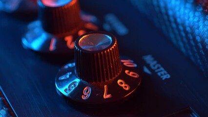guitarist's hand fine-tunes a dusty master volume knob on an electric guitar amplifier, captured in a striking close-up. Colorful neon lighting