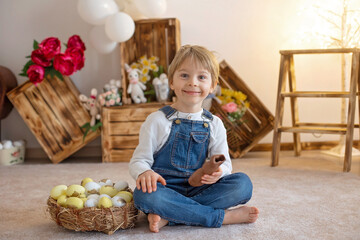 Sweet preschool boy in studio, playing with, egg for Easter and eating chocolate, child on Easter...