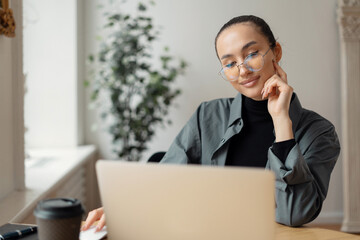 Contemplative young professional focused on a laptop in a bright office.