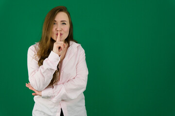 Portrait of flirty young woman making silence gesture over green background. Caucasian lady wearing posing with finger on lips. Silence and secret concept. High quality photo