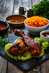 Roasted chicken drumsticks with sauerkraut and grated carrot on stony black plate on wooden table
