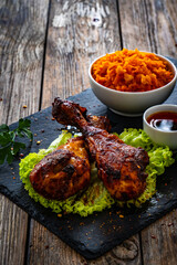 Roasted chicken drumsticks with sauerkraut and grated carrot on stony black plate on wooden table
