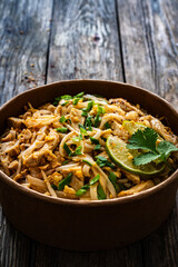 Pad Thai with chicken nuggets and rice noodles in peanut and tamarind sauce on wooden table in eco bowl to go
