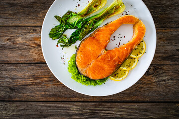 Fried salmon steak with lemon and steamed pak choi cabbage served on wooden table
