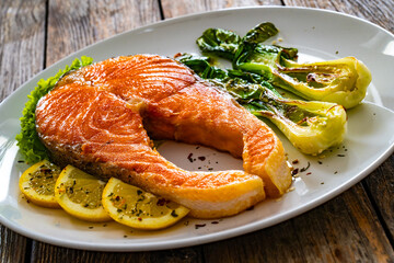Fried salmon steak with lemon and steamed pak choi cabbage served on wooden table
