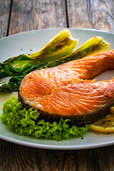 Fried salmon steak with lemon and steamed pak choi cabbage served on wooden table
