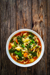 Pistou soup Nice - broth with basil pesto, noodles and vegetables on wooden background in white bowl