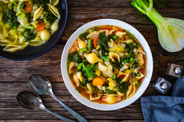 Pistou soup Nice - broth with basil pesto, noodles and vegetables on wooden background in white bowl