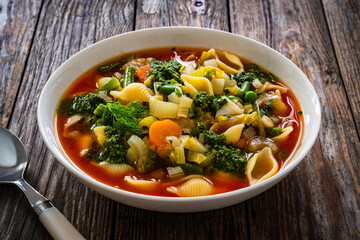 Pistou soup Nice - broth with basil pesto, noodles and vegetables on wooden background in white bowl
