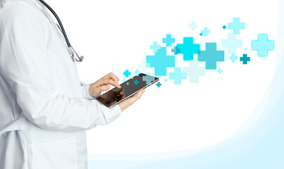 Doctor in a white coat on a light background with a tablet in his hands, blue and blue crosses. Medical Photography with Infographic, Crosses Flying Out of Tablet, Treatment and Health Care Concept