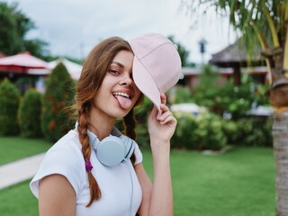 Fototapeta premium Teenage girl school in a pink cap with a backpack and headphones in a white T-shirt goes to school in college smile with teeth