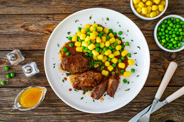 Baked pork cheeks in sauce with gnocchi and green peas on wooden table
