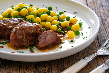 Baked pork cheeks in sauce with gnocchi and green peas on wooden table

