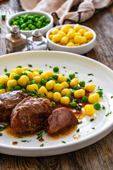 Baked pork cheeks in sauce with gnocchi and green peas on wooden table
