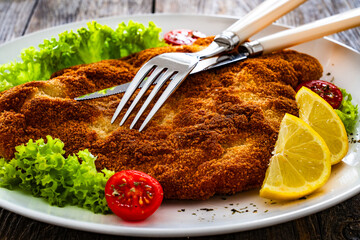 Crispy breaded fried pork chop and fresh vegetables on wooden table
