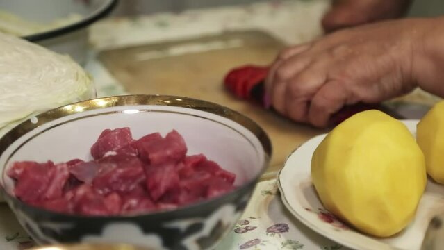 Hands of an elderly woman cutting peppers on a cutting board.