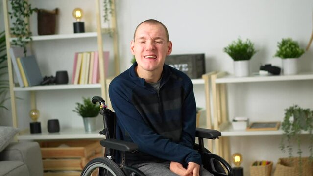 Portrait of a cheerful disabled man in wheelchair smiling at camera chilling at home
