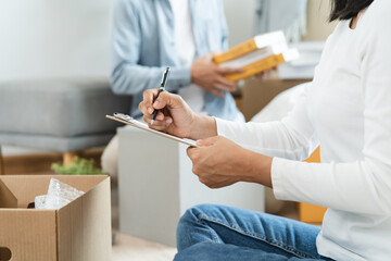 Happy woman checking stuff in cardboard box before sent to transportation company and moving to new...