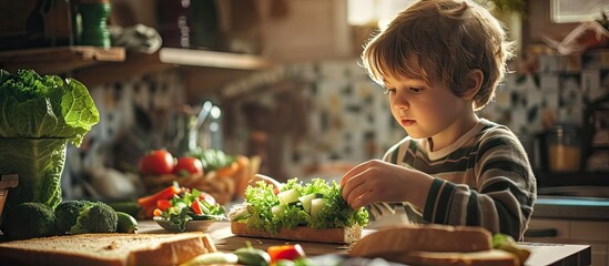 Cute little boy making vegetable sandwich with fresh ingredients he places lettuce on bread in kitchen at home. Creative Banner. Copyspace image - obrazy, fototapety, plakaty