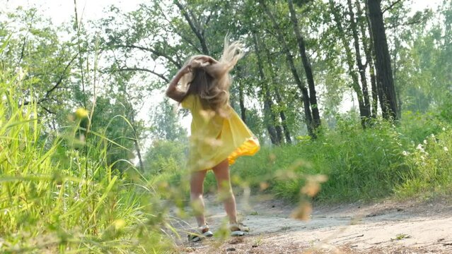 Happy little girl with blond long hair in a yellow dress and running along path on meadow with sunset	