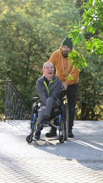 Caregiver pushing the wheelchair of a smiling disabled man in an urban park