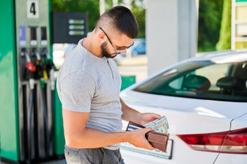 Man waiting for petrol station operator to pay for fuel. Handsome man near his car counting how...