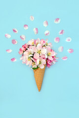 Surreal ice cream cone with apple blossom flowers and petals. Fun quirky food surrealistic abstract design for Spring, Easter, birthday, mothers day, logo or label on pastel blue.
