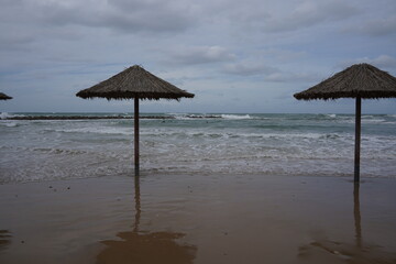Sandy beach in winter. Waves flood the sandy shore with umbrellas.