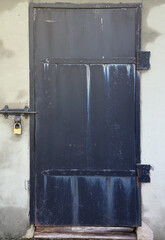 Black old metal door texture with iron handle and concrete wall. Outdoors texture close up