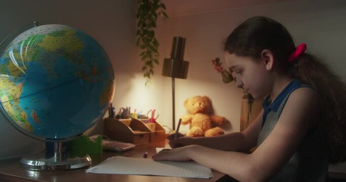 Cute smart school age girl learning to write, doing math homework, sitting at home desk, adorable cute school girl studying at home alone, doing math calculations, kids elementary education concept