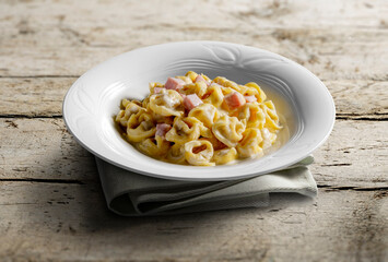 Tortellini soup bowl with cream and ham on wooden table