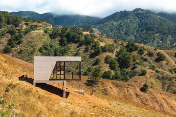 An isolated modern architectural structure stands in contrast to the vast, hilly terrain of a mountainous landscape. At San Nicolas, Pangasinan, part of the Cordillera mountains.