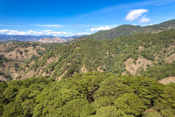 Elevated view of a verdant mountain landscape, dotted with green forest canopies and rugged terrain under a sunny sky. At Malico, Nueva Viscaya, part of the Cordillera mountains.