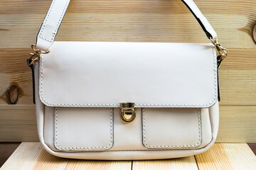 White leather women's handbag with a strap on a light wood background. elegant accessory for...