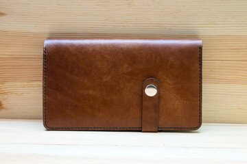 Men wallet made of rough brown leather on a light wood background. A stylish accessory for men,...