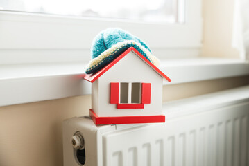 house in winter - heating system concept and cold snowy weather with model of a house wearing a...