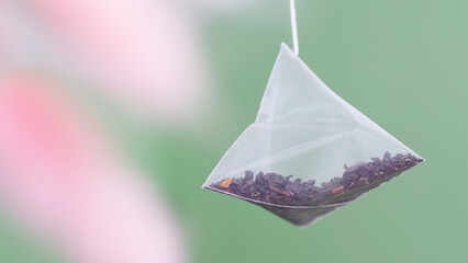 Triangular pyramid tea bag on gradient green-pink defocused background. Photo. Macro. Selective...