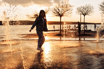 A little beautiful girl runs happily in torn jeans with long flowing hair against the background of a golden sunset.