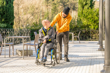 Caregiver pushing the wheelchair of a smiling disabled man outdoors