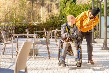 Happy disabled man and friend talking walking along urban park