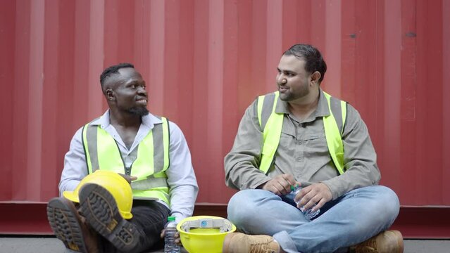 Two people African American and asian construction workers Happy Sit and rest in the container area and talking to during their break from work construction. foreman gives advice with subordinate